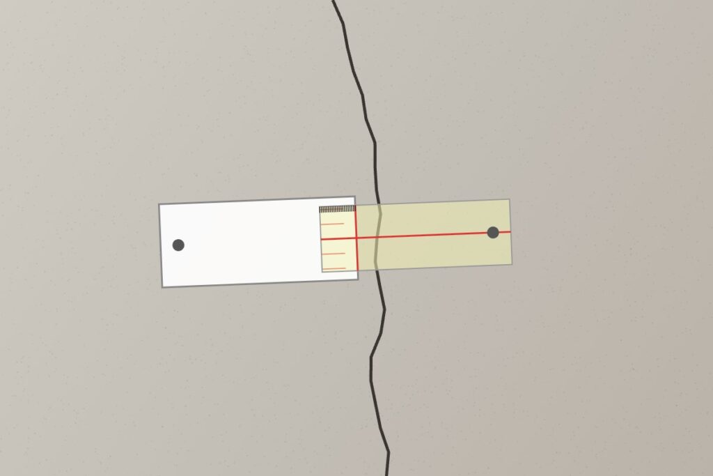 Plastic crack monitor fixed across a foundation crack to track movement